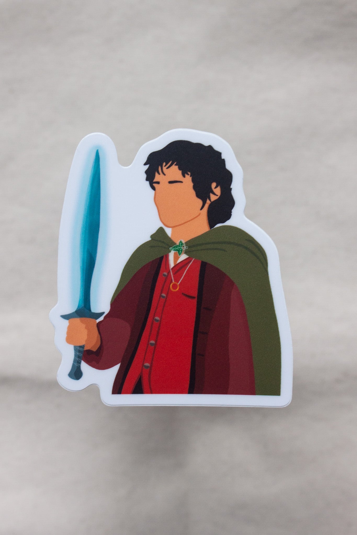 Frodo Baggins sticker from The Lord of the Rings, featuring the brave hobbit holding the One Ring with a determined expression. Perfect for fans of Frodo and Tolkien’s epic fantasy.